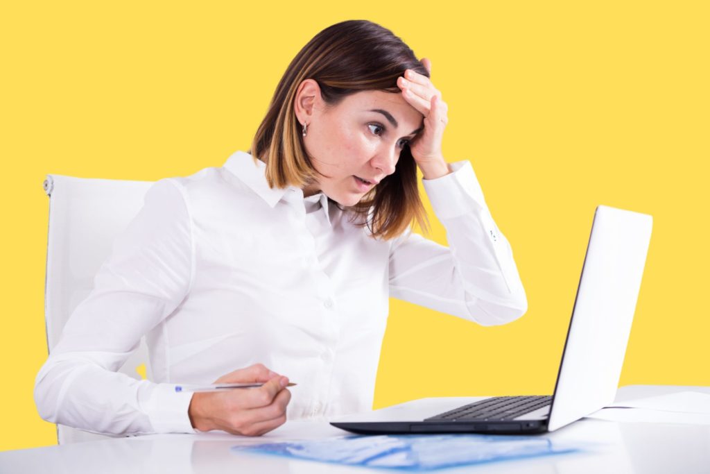 a woman in front of a laptop, with her hand on her forehead