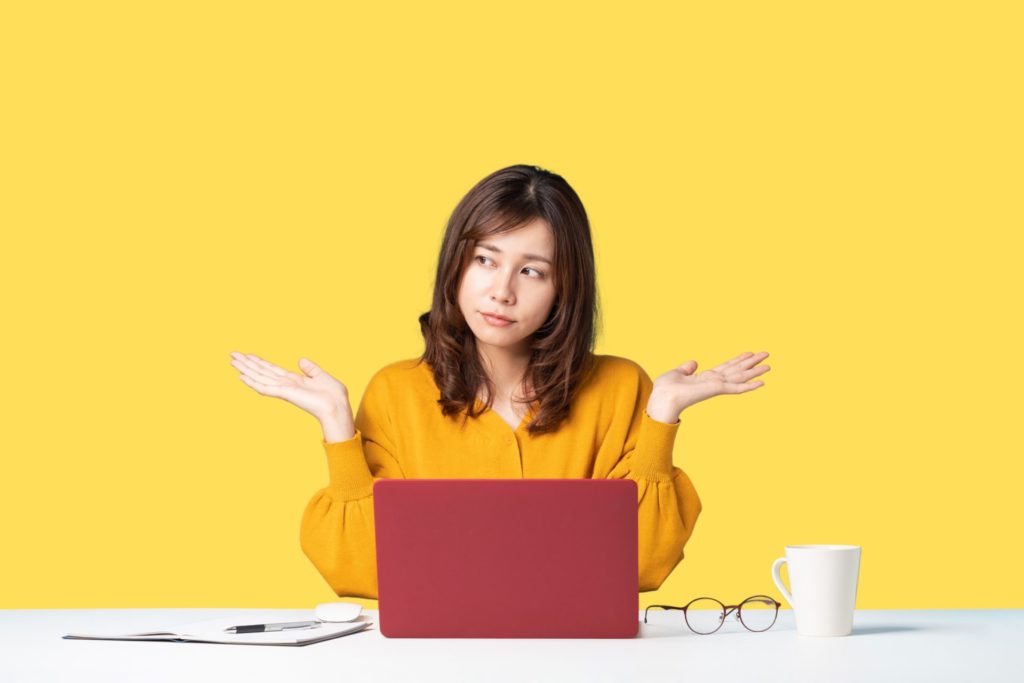 A confused woman sitting in front of a laptop with both hands pointing outwards