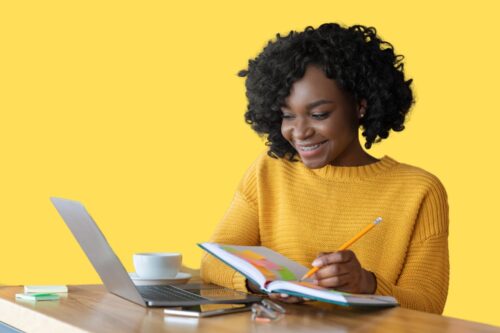 A woman in front of a laptop, writing in a notebook.