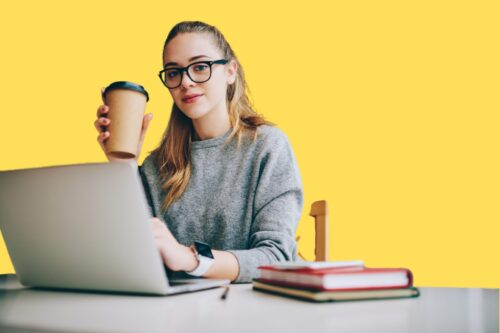 A woman sitting in front of a laptop, with a paper coffee cup in her hand