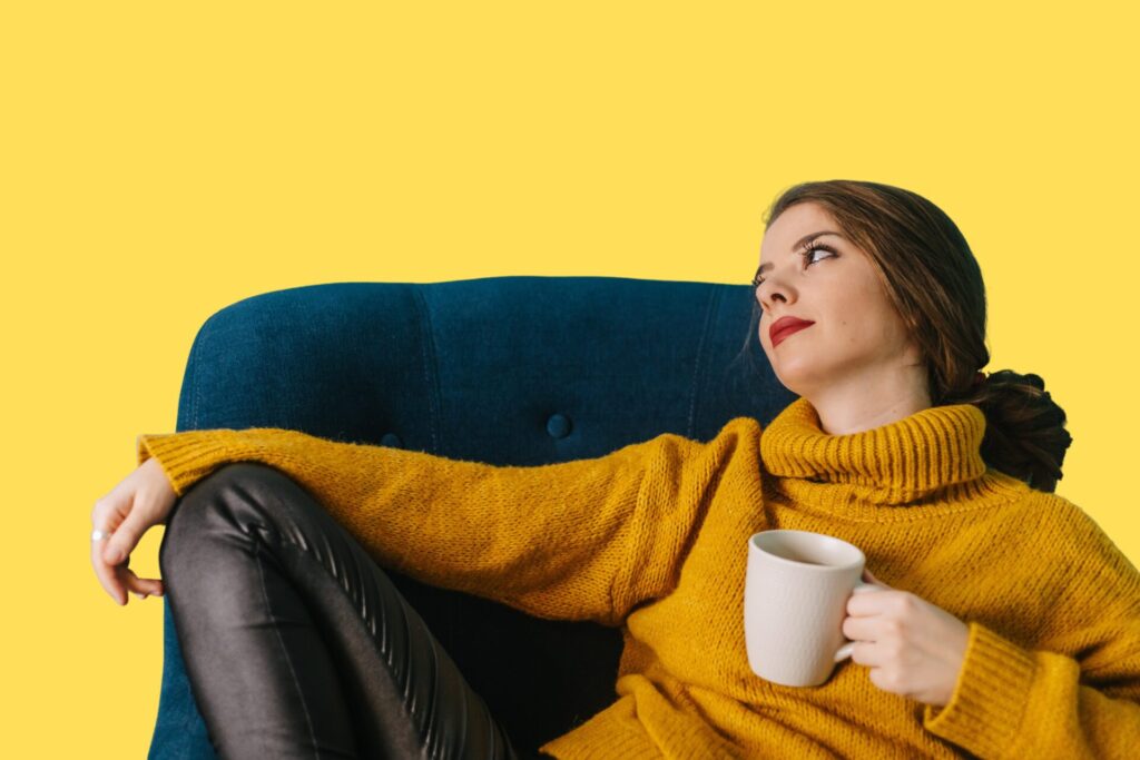 A woman contemplating, slouched on a couch with a mug in her hand