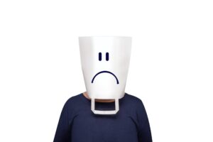 A man wearing a bucket on his head, with a sad face drawn on it